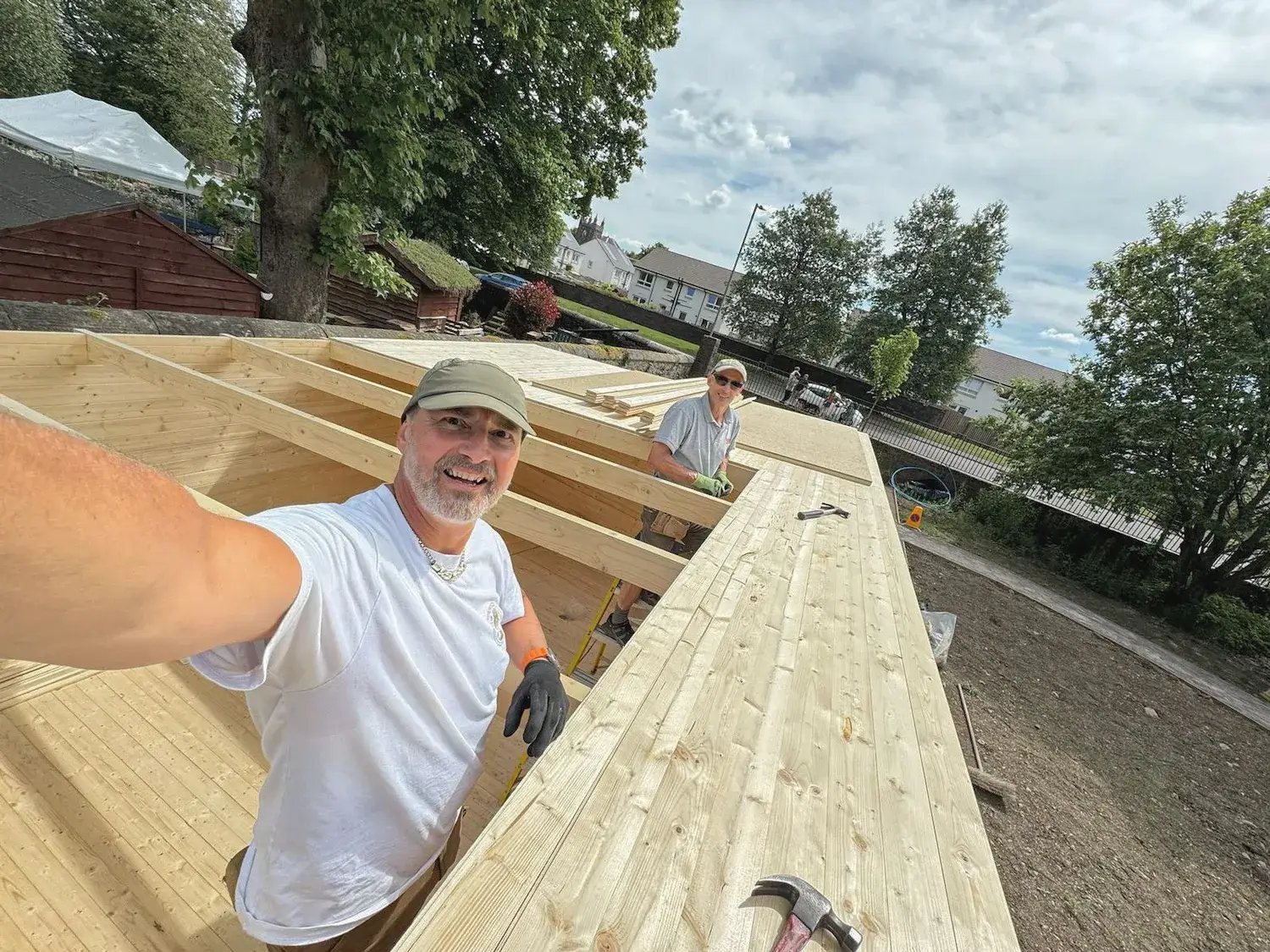 A high-angle selfie of two Men’s Shed members working together on the exposed timber roof frame during the construction of their original wooden cabin shed.