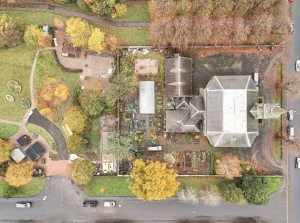 Flat, top-down aerial view of the Lochwinnoch Parish Church complex, showing the slate-roofed church and halls at the rear, connecting to the rectangular walled community garden, which sits adjacent to Lochhead Gardens behind a stone wall.