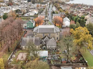 Overhead aerial view looking down on the Lochwinnoch Parish Church complex, showing the main building, interconnected halls, and a walled rear yard containing the community garden and behind that, Lochhead Gardens